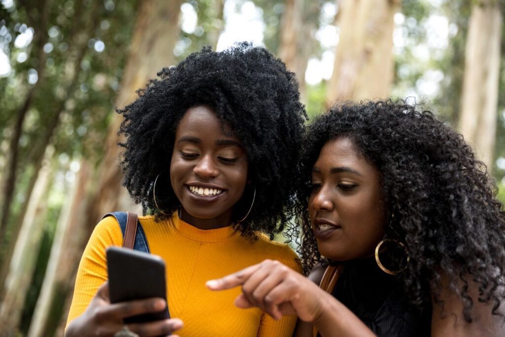 Two women looking at a cell phone in the woods.