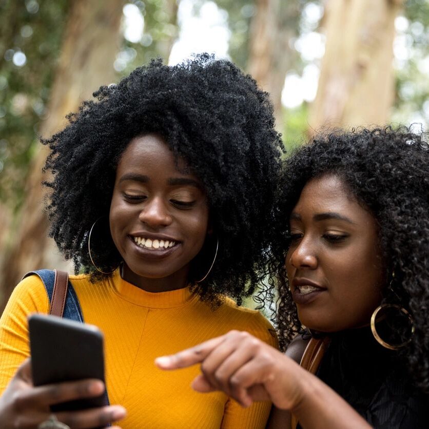 Two women looking at a cell phone in the woods.